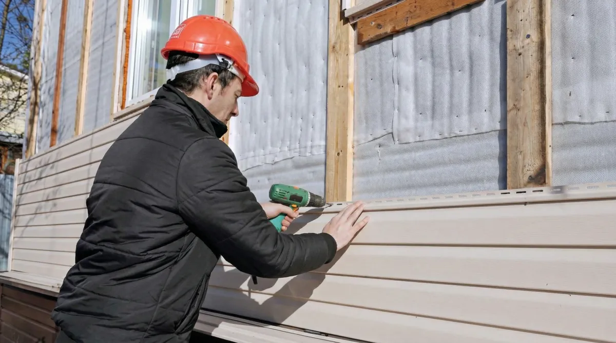 Siding replacement professional using a power drill to install new tan vinyl siding on a home exterior in Scottsdale, AZ